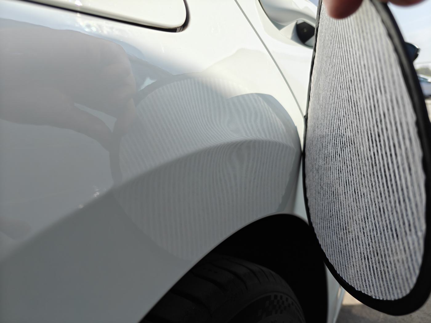 Prüfung einer Delle am hinteren Kotflügel eines weißen Fahrzeugs mit einer Streifen-Reflexionsscheibe